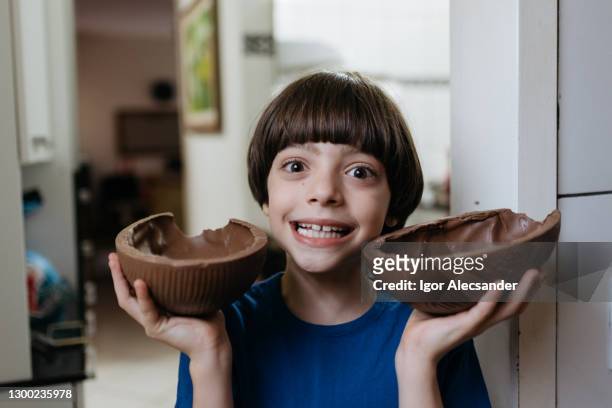 boy holding two halves of an easter egg in the kitchen - funny easter stock pictures, royalty-free photos & images