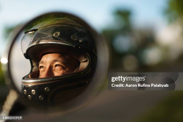 southeast asian man's happy eyes inside motorcycle helmet reflected on side mirror - crash helmet fotografías e imágenes de stock