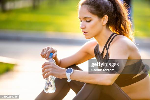 young woman sitting on the ground with water bottle on a break from running - open practice stock pictures, royalty-free photos & images