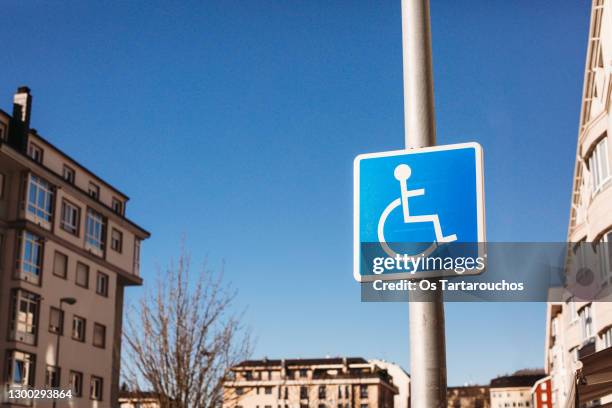 disabled parking sign attached to a lamppost in the city with buildings in the background - handicap photos et images de collection