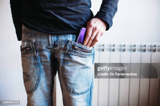 mid section close up of a man's hand putting the smartphone in his front pocket - hands in pockets foto e immagini stock