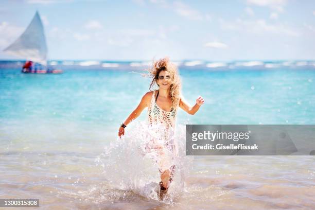 mujer madura despreocupada en ropa de playa salpicando en el agua en la playa - porto galinhas fotografías e imágenes de stock
