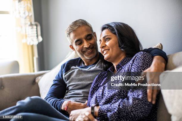 husband and wife embracing on couch - mature couple lifestyle stock pictures, royalty-free photos & images