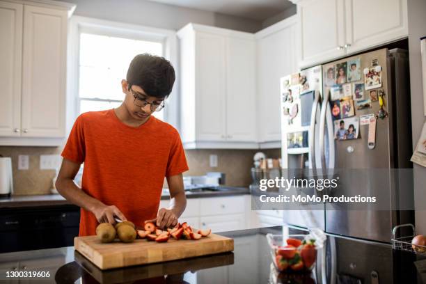 high school boy cutting fruit in kitchen - teenager cooking stock pictures, royalty-free photos & images