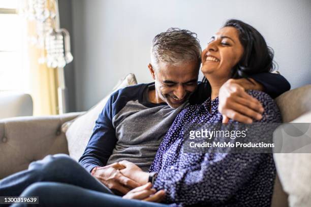husband and wife embracing on couch - couple photos et images de collection