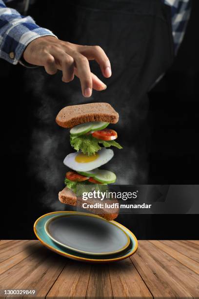 a flying sandwich on a plate consisting of toast. cucumber, fried egg, tomato - munandar stock pictures, royalty-free photos & images