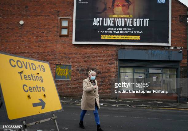 Woman walks past a Covid-19 testing site direction sign and a government pandemic poster in the Leamore area of Walsall as mass testing is started to...