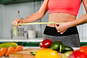 Healthy fit girl measuring her waist with measuring tape in the kitchen