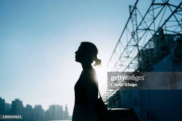 silhouette of confident and ambitious young asian woman standing against urban cityscape with giant framework of advertisement billboard sign in city, looking towards sky on a fresh bright morning. female leadership and determined to success - dreams foundation stock pictures, royalty-free photos & images