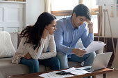 Concerned young married couple studying bank letters informing about debt