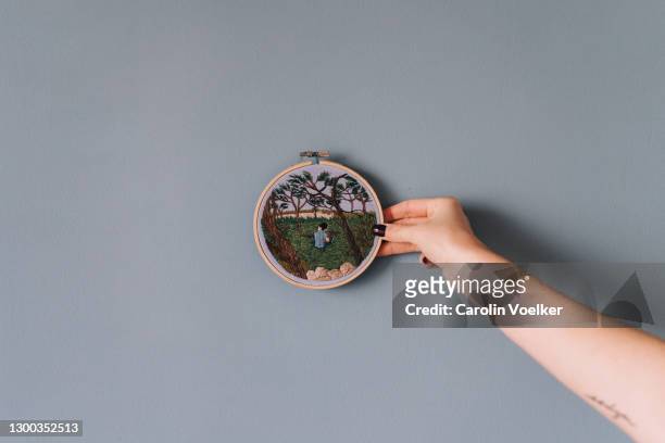 female hand holding up a craft product to a colourful wall - embroidery frame stock pictures, royalty-free photos & images