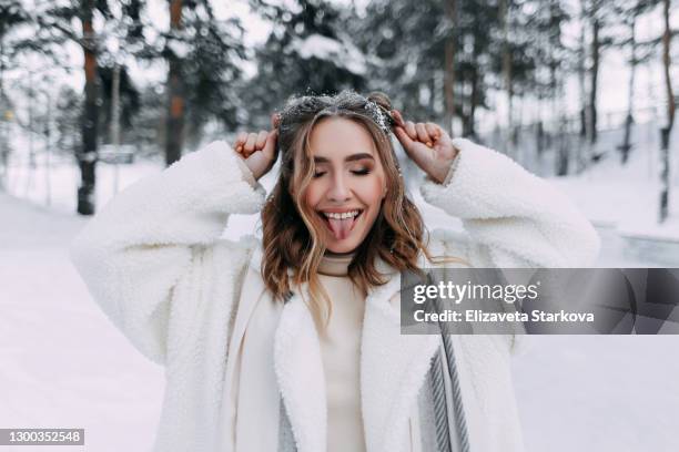 close-up portrait of a happy cheerful playful emotional laughing cute girl in a warm fur coat and scarf walks, has fun and grimaces in a snowy forest - freeze motion stock-fotos und bilder