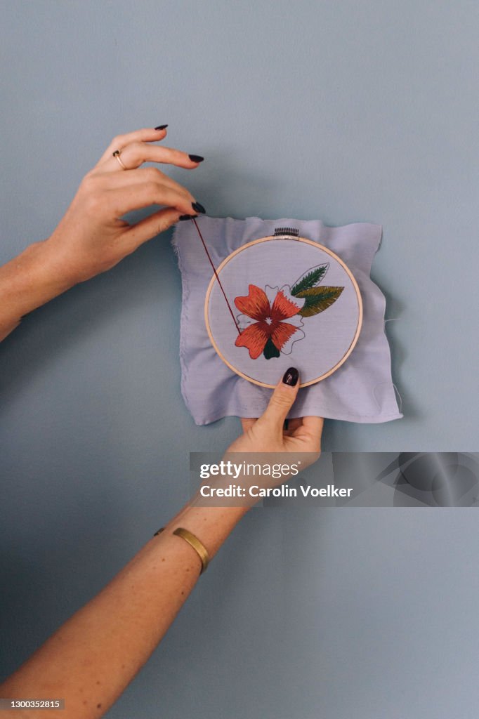 Two hands doing embroidery in front of a blue wall