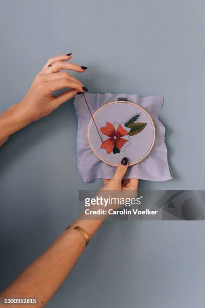 two hands doing embroidery in front of a blue wall - embroidery frame stock pictures, royalty-free photos & images