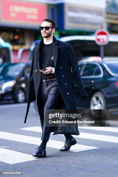 Pelayo Diaz wears Ray Ban sunglasses, a black long wool trench coat, a white shirt, a black wool pullover, a gold ring, black suit pants, black...