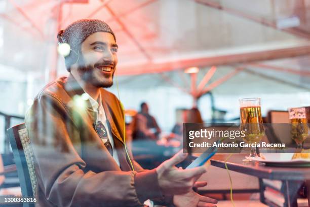young man listening music in bar terrace. night life, winter terrace outdoors with protective glass - jaén city stock pictures, royalty-free photos & images