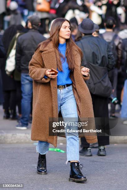 Guest wears a camel fluffy oversized coat, a royal blue turtleneck wool pullover, a gold Gucci double G leather belt, denim ripped mom jeans, Dr...