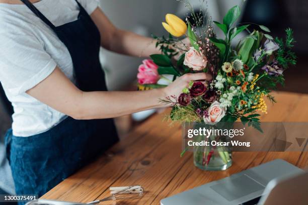 cropped shot of young woman arranging fresh flowers at home - arreglo floral fotografías e imágenes de stock