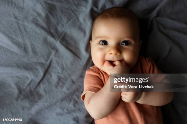 small beautiful child lies on the bed on his stomach and smiles. happy toddler girl boy on dark bedspread at home - baby happy cute smiling baby only stockfoto's en -beelden