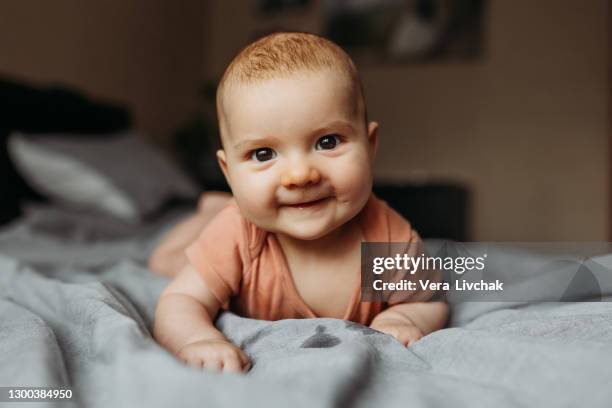 small beautiful child lies on the bed on his stomach and smiles. happy toddler girl boy on dark bedspread at home - diaper girl stock pictures, royalty-free photos & images