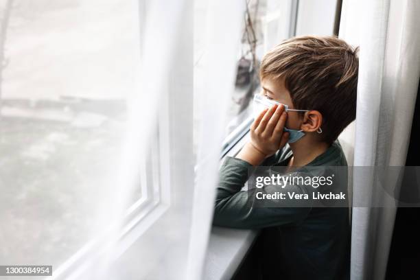 small sad boy looking through the window during coronavirus isolation. - coronavirus russia stock pictures, royalty-free photos & images