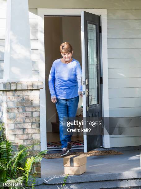 senior woman opens front door to get delivery from porch - stoop stock pictures, royalty-free photos & images