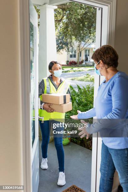 senior woman opening front door for home delivery, masks - answering door stock pictures, royalty-free photos & images