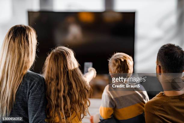 vista trasera de una familia viendo la televisión en casa. - familia viendo television fotografías e imágenes de stock