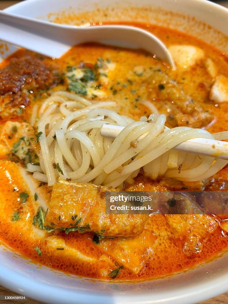 Directly above shot of hand holding chopsticks, eating creamy Singaporean laksa.