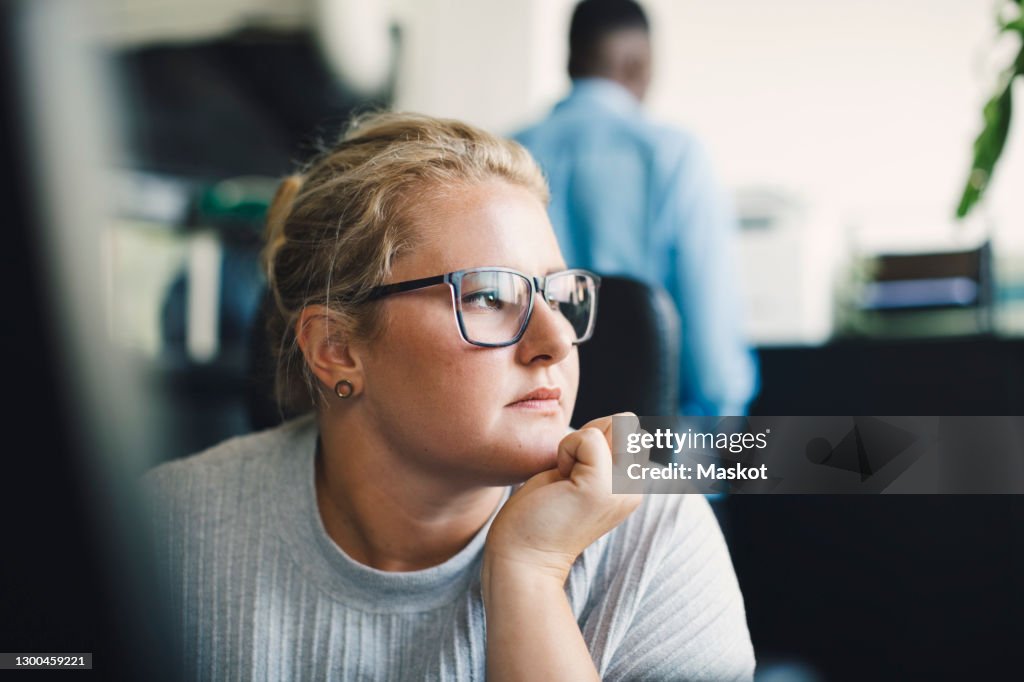 Female entrepreneur with hand on chin looking away in office
