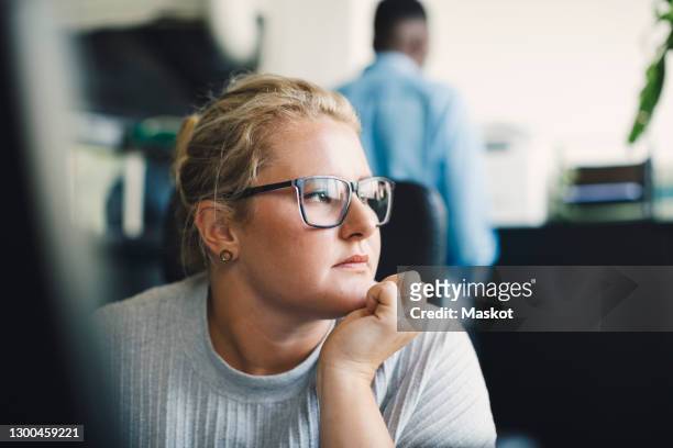 female entrepreneur with hand on chin looking away in office - lässig schicker stil frau stock-fotos und bilder