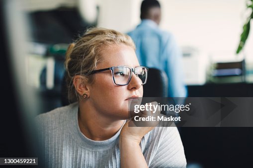 Female entrepreneur with hand on chin looking away in office Female entrepreneur with hand on chin looking away in office