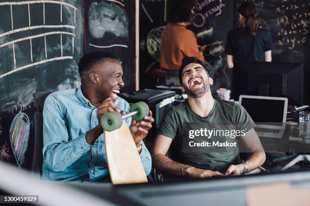 cheerful it professionals laughing while sitting with skateboard at office - laugh fotografías e imágenes de stock