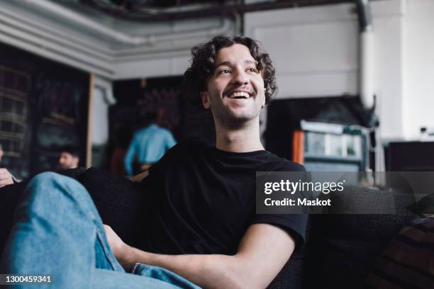 smiling male engineer looking away while sitting on sofa in office - office sofa stock-fotos und bilder