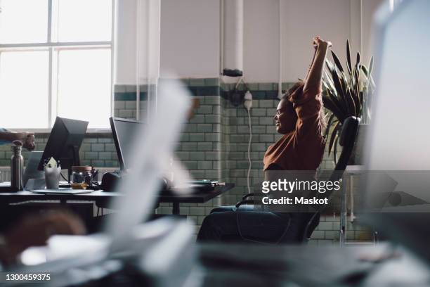 young businesswoman stretching with hand raised while sitting on chair in office - yawn office stockfoto's en -beelden