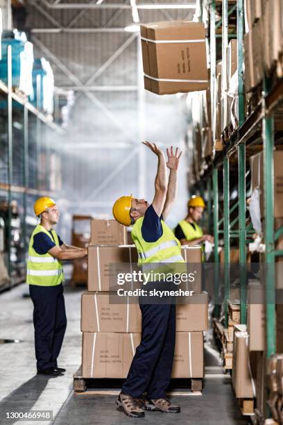 jonge pakhuisarbeider die kartondoos in industrieel gebouw vangt. - catch stockfoto's en -beelden