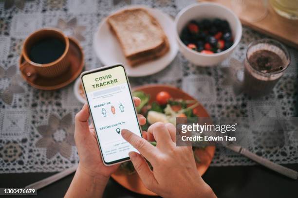 high angle view asian chinese woman's hand on mobile app covid 19 mobile app tracker on latest update and check in status  during breakfast time - spy hunter stock pictures, royalty-free photos & images
