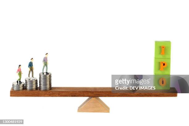 stack of coins and ipo blocks balancing on seesaw - capitalism stock pictures, royalty-free photos & images