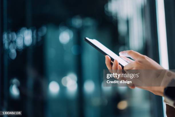 close up of young woman using smartphone on the go, against contemporary city buildings with illuminated facade at night. the smartphone on hand is in blank screen for mobile app mockup design - hand paying smartphone stock pictures, royalty-free photos & images