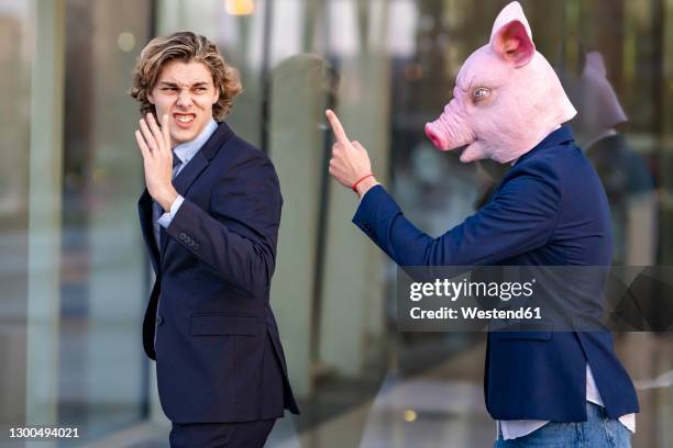 young businessman in pig mask arguing with male colleague by glass wall - mask irritation stock pictures, royalty-free photos & images