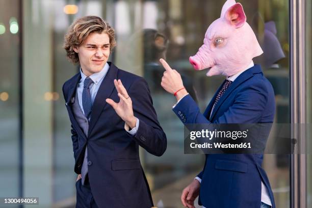 businessman in pig mask pointing and arguing with male coworker by glass wall - dissent collar stock pictures, royalty-free photos & images