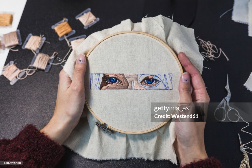 Hands of young woman holding embroidery frame on table in studio