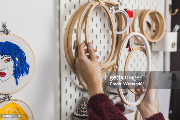 hands of young woman holding embroidery frames hanging on wall in studio - embroidery frame stock pictures, royalty-free photos & images