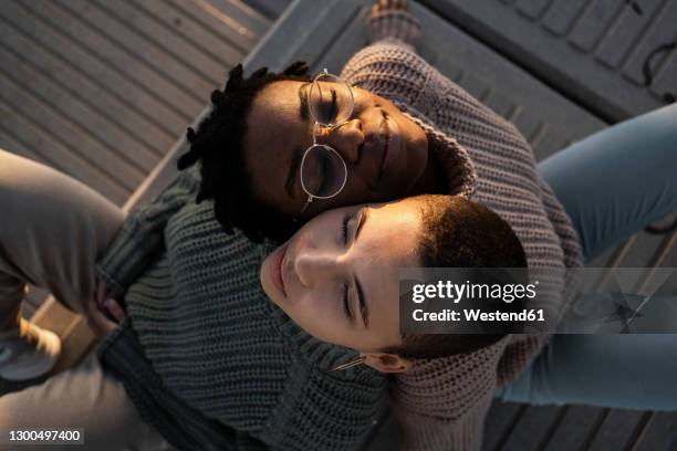 young women leaning on each other shoulder while sitting on bench - leunen stockfoto's en -beelden