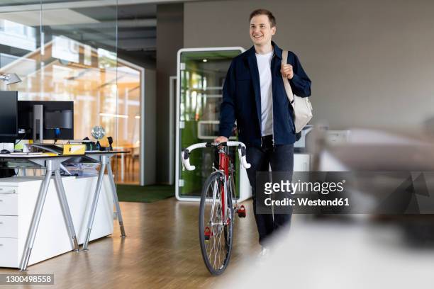 smiling businessman with bag and bicycle walking while leaving after work from office - feierabend stock-fotos und bilder