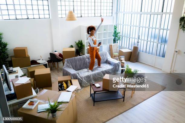 afro woman dancing on sofa while listening music through headphones in new apartment - music box 個照片及圖片檔