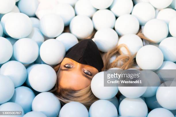 close-up of young woman wearing face mask lying in ball pit - adult ball pit stock-fotos und bilder