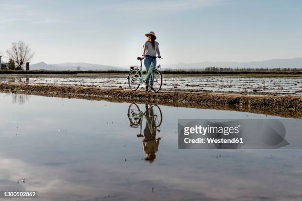 young woman standing with bicycle against sky at ebro's delta during vacations, spain - ebro river - fotografias e filmes do acervo