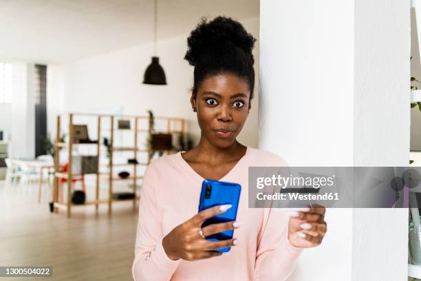 surprised woman with credit card and mobile phone staring while standing at home - staring stock pictures, royalty-free photos & images