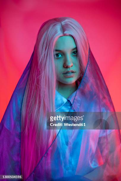 close-up of serious young woman wearing wig with scarf against pink background - straight hair stock pictures, royalty-free photos & images